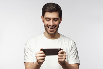 Caucasian guy feeling excitement with multimedia content from Internet he is watching on cellphone, isolated on gray background