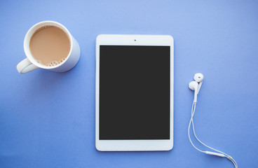 Flat lay of white tablet, earphones and a cup of coffee on purple background with copyspace.