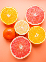 Flat lay of cut ripe juicy grapefruit, lemon and orange on orange color background.