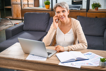 Mature businesswoman talking by phone in office