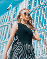 Beautiful girl in glasses and a handbag posing on the background of a high iron fence