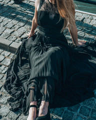 Beautiful girl in a black dress sits on the bridge