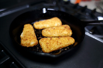 Breaded fish sticks baked in a cast iron skillet, resting on the stove.
