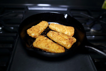 Breaded fish sticks baked in a cast iron skillet, resting on the stove.