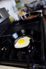 Egg frying, sunny side up,  in a cast iron skillet with corned beef hash in the background,  on a natural gas stove top in a home kitchen. 