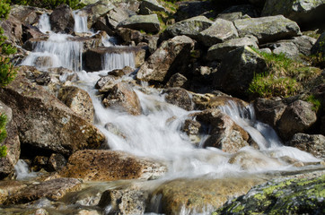 A stream in the mountains flows along the rocks and a stormy waterfall