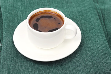 white Cup of black coffee rests on denim pants.
