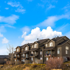 Square frame Houses with balconies and arched windows against blue sky with puffy clouds