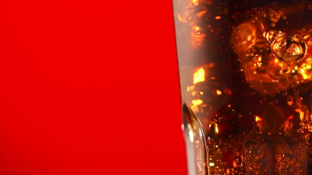Coke with ice cubes closeup. Glass of fizzy cola rotated over red background. 4K UHD video footage. 3840X2160