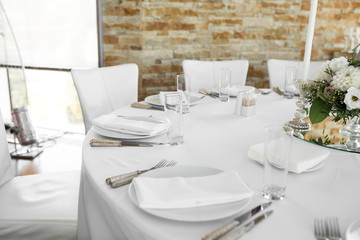 Wedding table setting decorated with fresh flowers. White plates, silverware, white tablecloth and white room. Wedding floristry. Banquet table for guests. Bouquet with roses, hydrangea and eustoma
