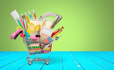 Variety office supplies in little shopping cart on wooden table  on background