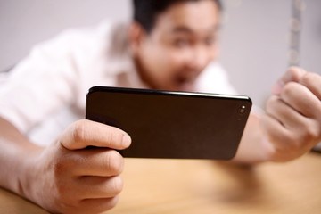 Funny Young Asian Guy Playing Games on Tablet Smart Phone