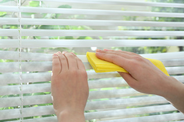 Woman wiping window blinds with rag indoors, closeup. Before and after cleaning