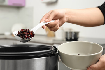 Woman putting brown rice into bowl from multi cooker in kitchen, closeup