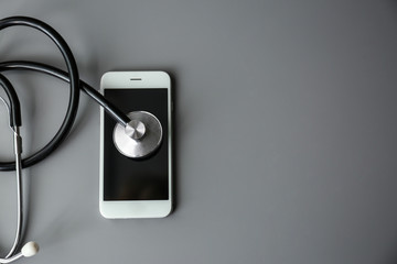 Fototapeta na wymiar Smartphone and stethoscope on grey table, top view with space for text. Repairing service