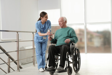 Fototapeta na wymiar Nurse giving water to senior man in wheelchair at hospital. Medical assisting