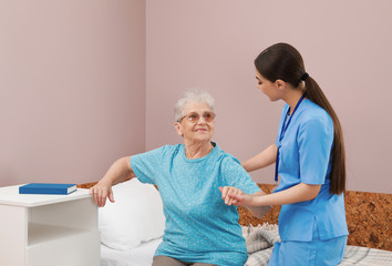 Obraz premium Nurse assisting senior woman on bed in hospital ward
