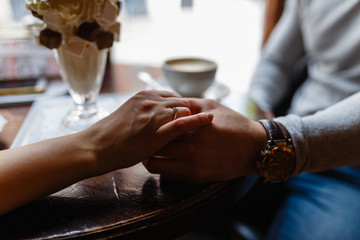 Young girl and young man holding hands on wooden table in cafe. A man and a woman holding hands in a cafe restaurant, a young couple enjoying a cozy cafe and each other, close-up