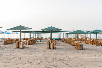 Many plastic deckchairs and umbrellas at the sea beach at sunrise. Summer vacation concept.