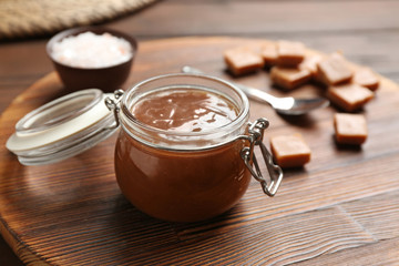 Jar of tasty caramel sauce on board, closeup