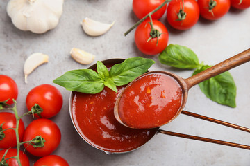 Flat lay composition with spoon and pan of tomato sauce on grey table