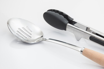 Slotted serving spoon and cooking tongs on white background.