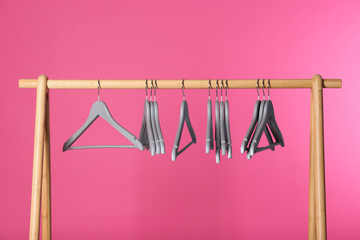 Wooden rack with clothes hangers on color background