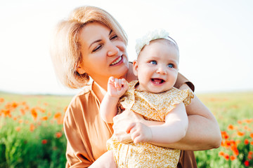 Grandmother with a little granddaughter playing in a poppy field.