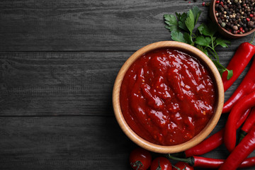 Flat lay composition with bowl of chili sauce and ingredients on wooden table. Space for text