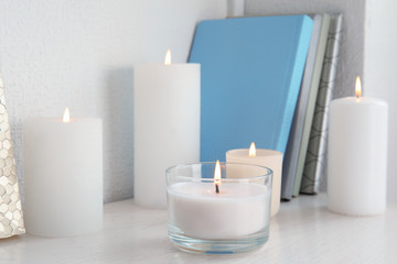 Fototapeta na wymiar Burning aromatic candles in holders on bookshelf