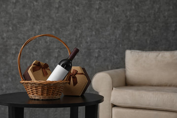 Wicker basket with bottle of wine and gift boxes on table in room. Space for design