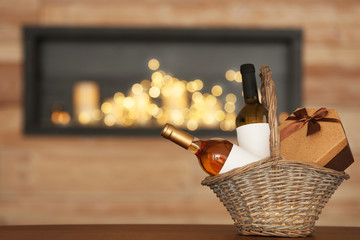 Wicker basket with bottles of wine and gift box on table in room. Space for text