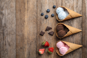 Flat lay composition with delicious ice creams in waffle cones on wooden table, space for text