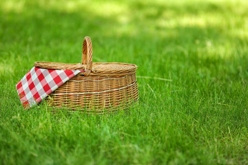 Wicker basket with blanket on green grass in park, space for text. Summer picnic