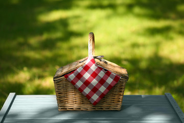 Wicker basket with blanket on table in park. Summer picnic