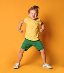 Kid boy in yellow t-shirt, green short and white sneakers is in a pose of angry monster...