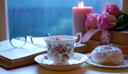Nostalgia scene relaxing by the window on a cold rainy day with old books and cup of tea.
