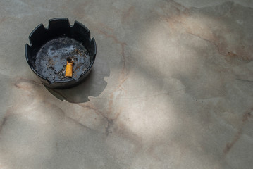 The black ceramic ashtray and the cigarette butts are extinguished oon the marble table.
