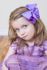 Little cute blonde Caucasian girl portrait . Girl is wearing in purple dress and purple bow in her hair