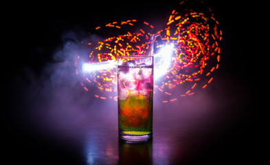 Cocktail glass splashing on dark toned smoky background or colorful cocktail in glass. Party club entertainment. Mixed light.
