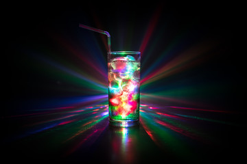 Cocktail glass splashing on dark toned smoky background or colorful cocktail in glass. Party club entertainment. Mixed light.
