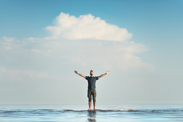 A man stands in shallow water. His hands are raised