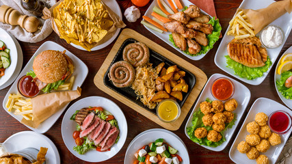 assorted sausages with sauces, burger, cheese balls, nachos, chicken wings, chicken breast, salad with roast beef, greek salad