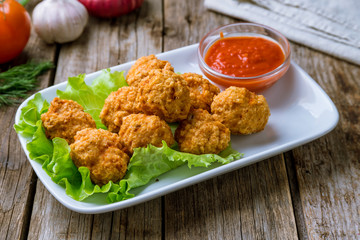 Chicken balls with ketchup on white plate on wooden background