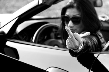 young woman shows middle finger out of car