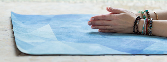 Young yoga woman rolling her blue mat after a yoga class on the floor, close up. Panoramic backdrop