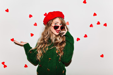 Amazing curly girl touching her sunglasses and expressing amazement in valentine's day. Studio shot...