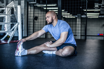 Naklejka premium Young man preparing muscles before training. Muscular athlete exercising in gym. Fit man stretching. Professional sportsman warming-up. Full body length portrait. dressed in a sports uniform.