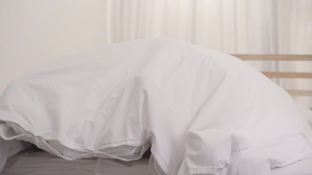 Asian couple lying on bed in bedroom, couple feeling happy having funny time playing under blanket together on bed at home. Couple relax enjoy love moment at home concept.