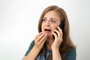 Young caucasian girl woman is talking on the mobile phone, looks scared or sad